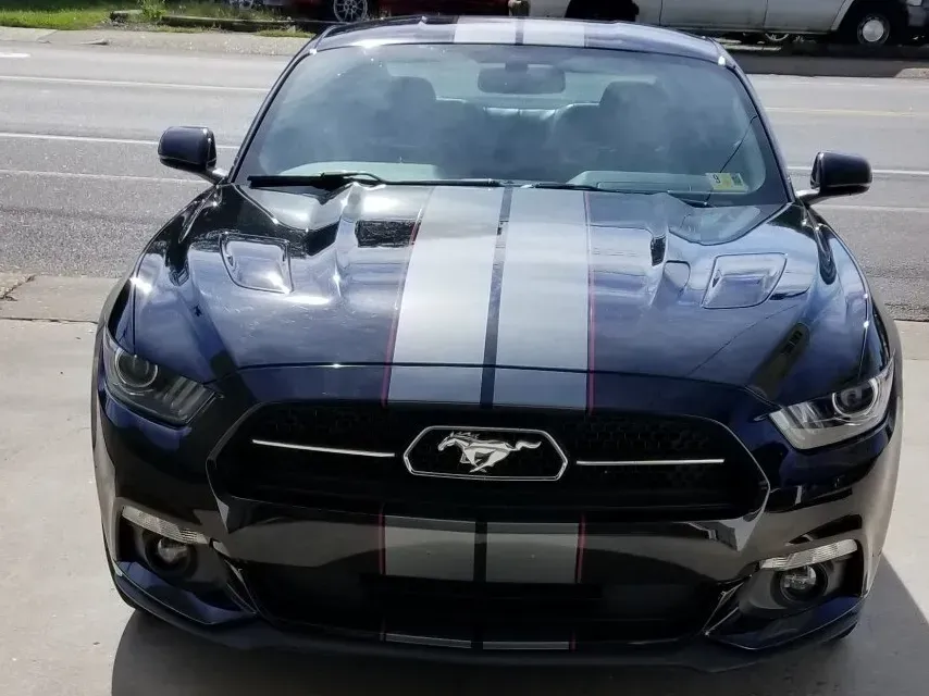 A black mustang with white stripes is parked on the side of the road.