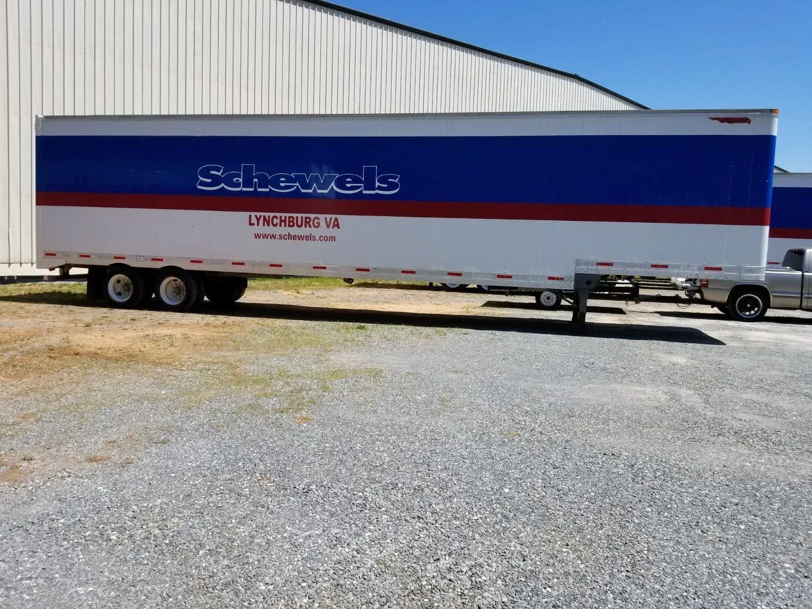 A blue and white semi truck is parked in a gravel lot.