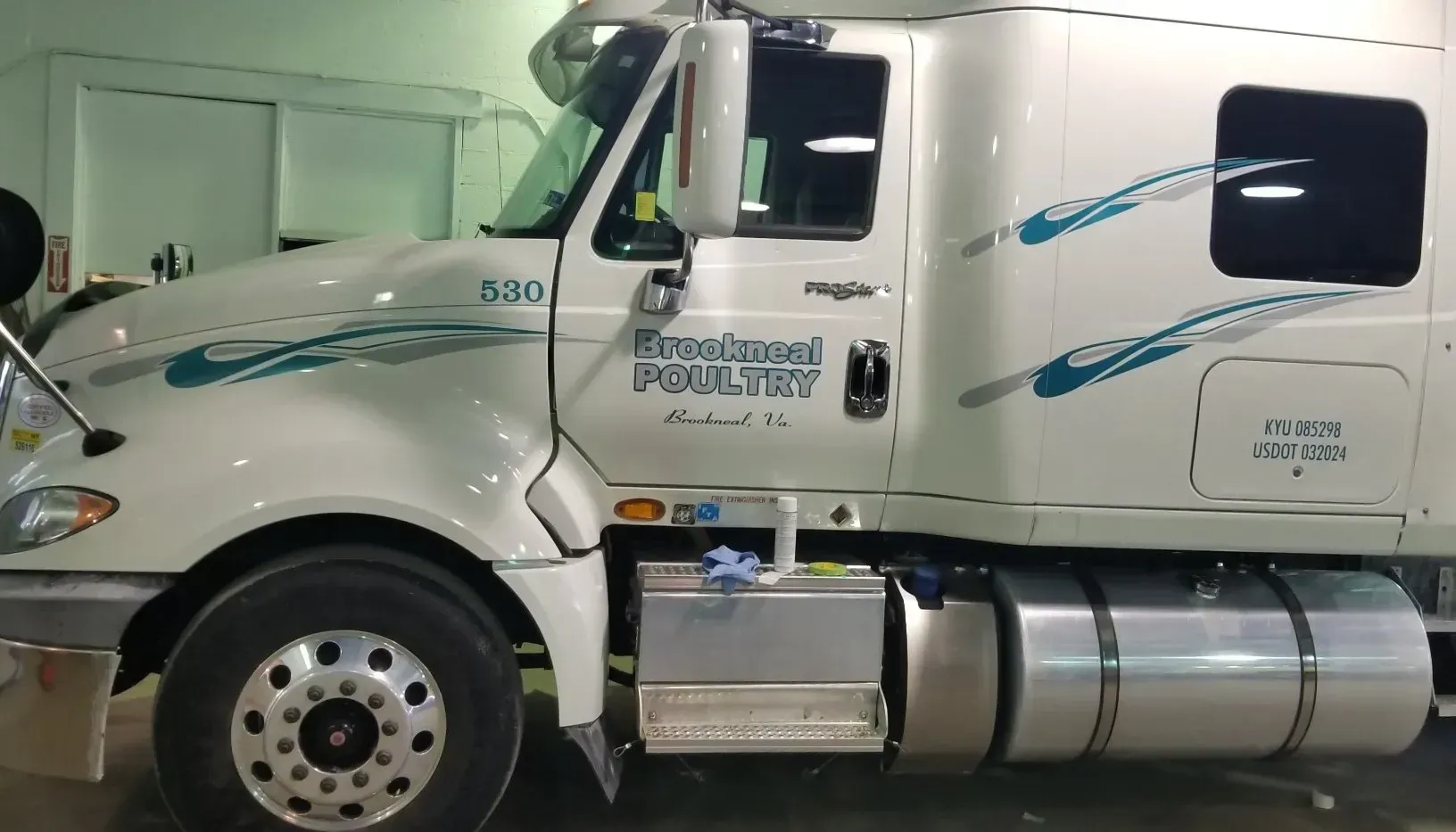 A white semi truck with a blue stripe on the side is parked in a garage.
