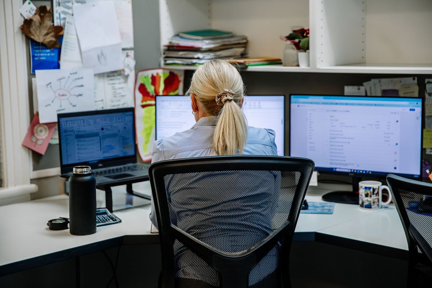 Person working at a desk with three computer monitors in an office cubicle