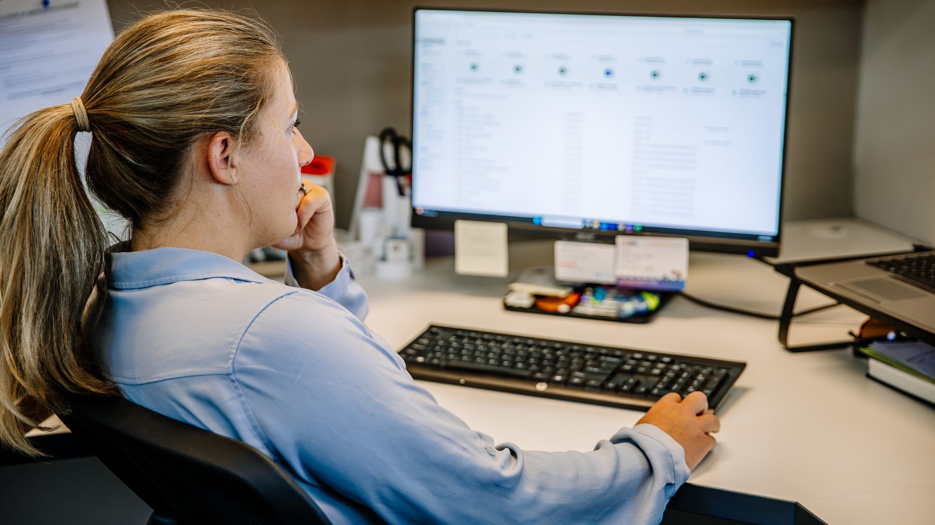 Person working at a desk with a computer monitor, keyboard, and mouse in an office setting.