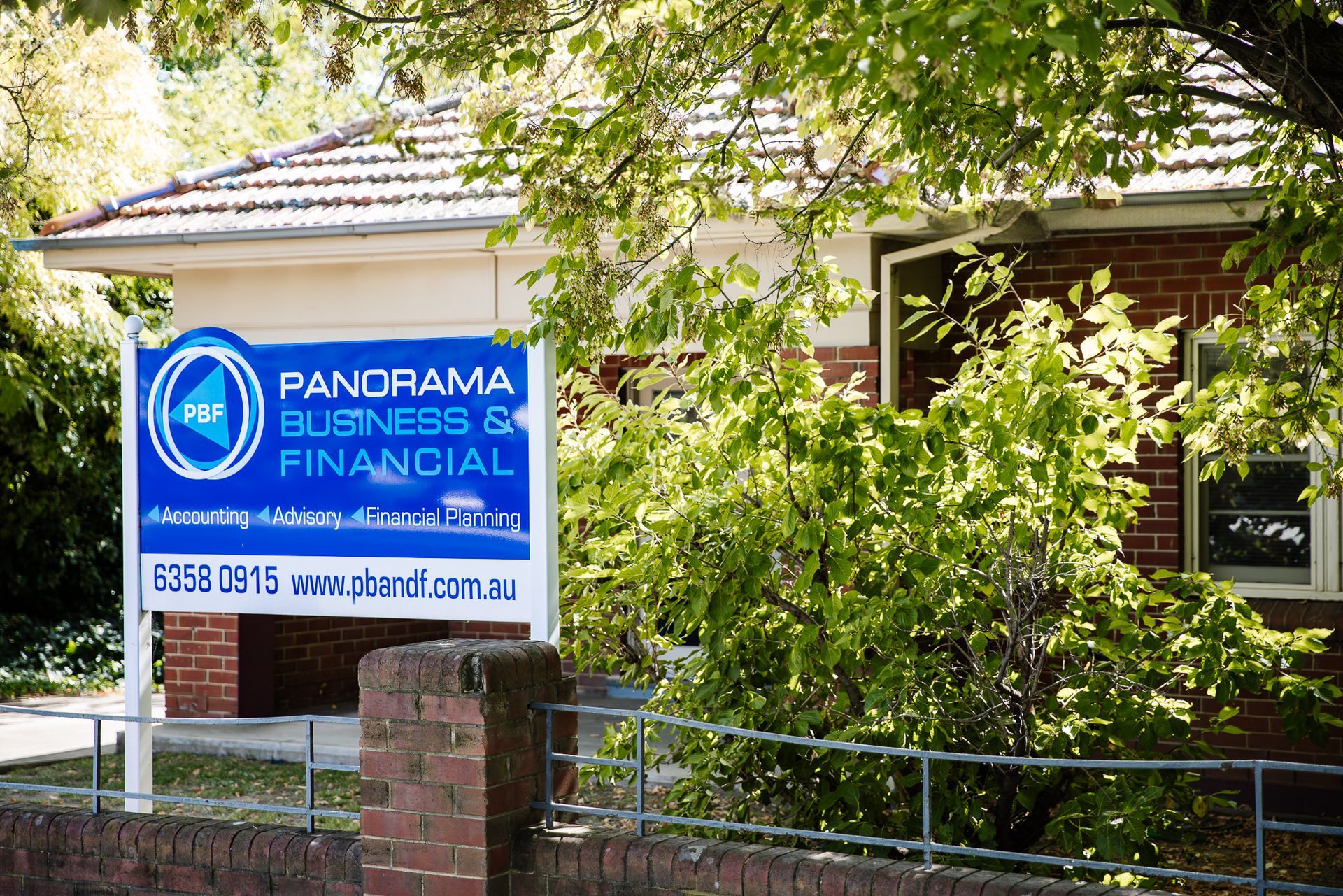 Panorama Business Financial sign outside a house, partly hidden by trees and a brick fence