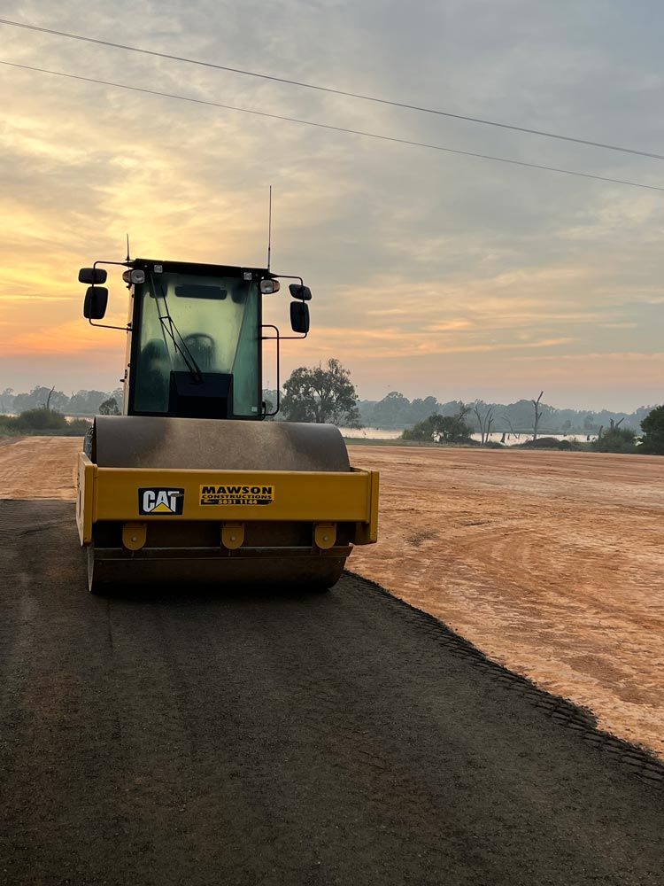 A Yellow cat Roller is Driving down a dirt road — Mawson Constructions in Kialla, VIC