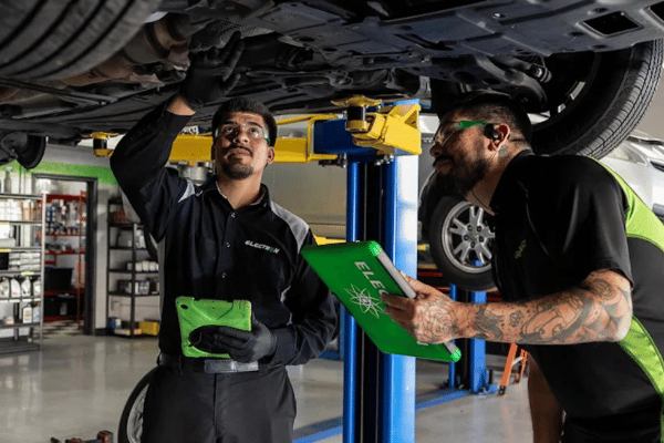 Two Electron Automotive technicians inspecting vehicle under lift with tablet