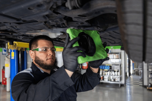Electron Automotive technician inspecting underside of vehicle with cloth