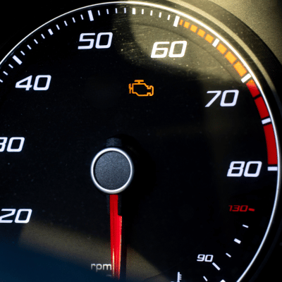 Dashboard with illuminated orange check engine light. Speedometer needle points near 60.