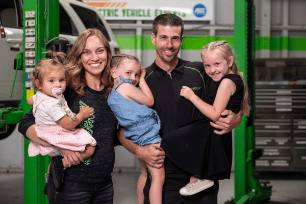 Chris and his wife holding their kids in the vehicle bay smiling at the camera