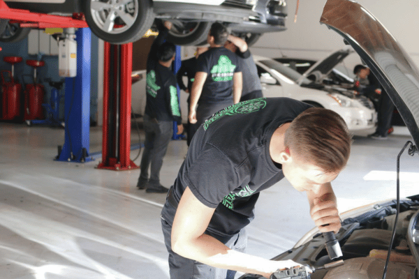 Electron Automotive technician inspecting engine with flashlight in repair shop