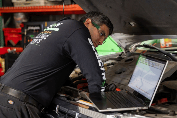 Electron Automotive technician diagnosing vehicle using laptop under hood