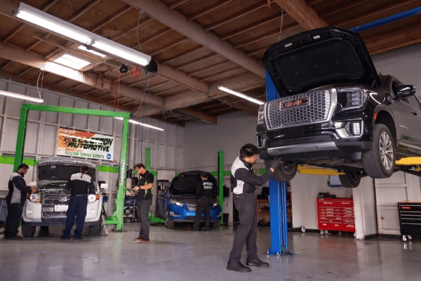 Electron Automotive shop with technician inspecting black GMC truck on lift