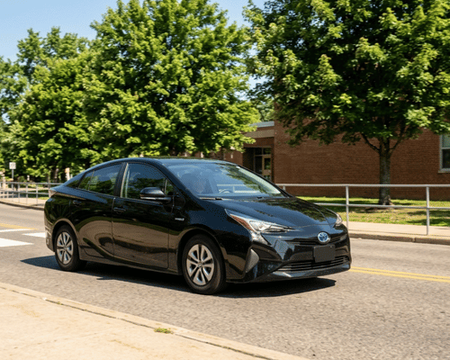 Black Toyota Prius hybrid driving near a school on a sunny day