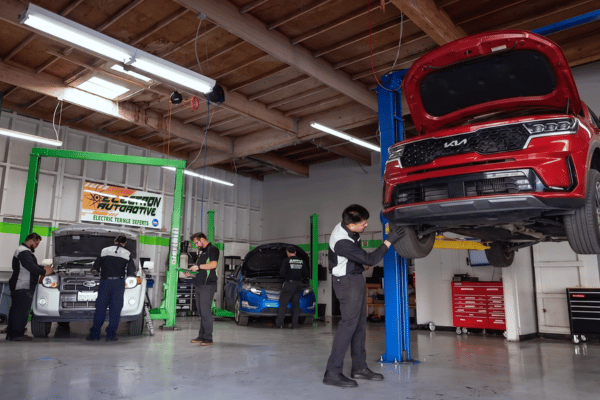 Electron Automotive shop with technician inspecting red Kia on lift