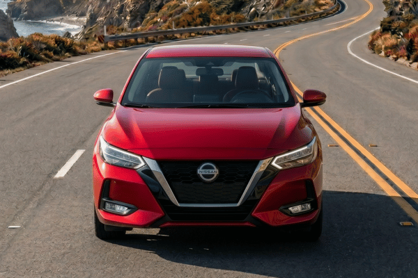 Red Nissan sedan driving on coastal road
