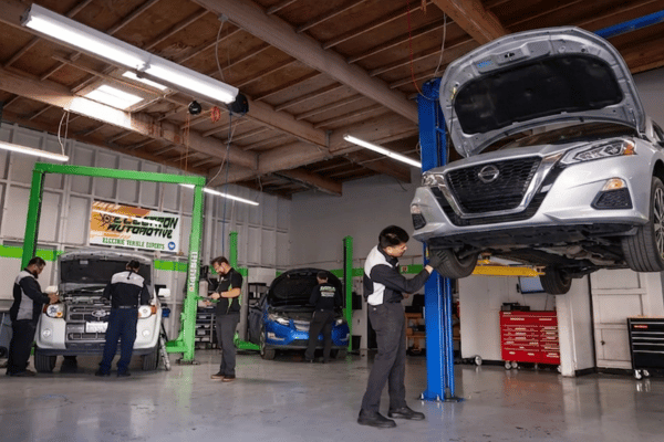 Electron Automotive shop with technician inspecting silver Nissan on lift