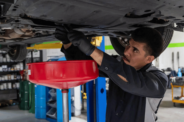 Electron Automotive technician draining oil from vehicle on lift