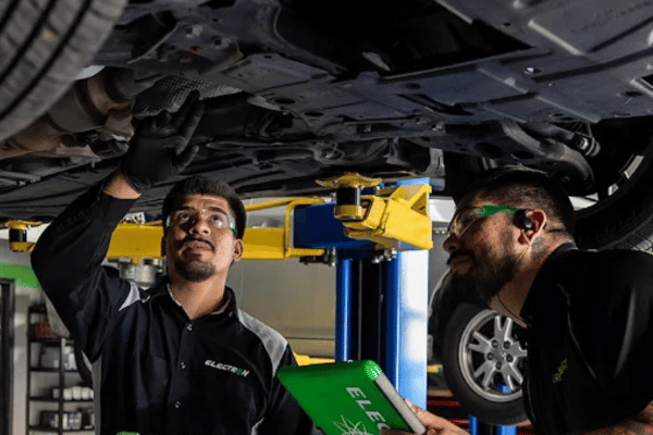 Two Electron Automotive technicians inspecting vehicle under lift with tablet