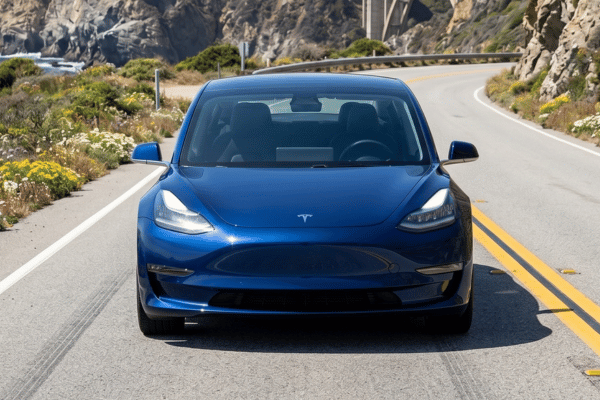 Blue Tesla sedan driving on coastal road