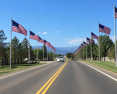 Car driving on a road lined with American flags, trees, and mountain views under a clear blue sky.