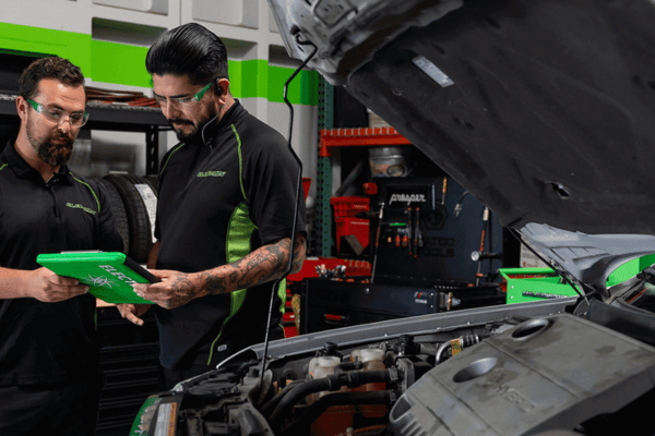 Two Electron Automotive technicians reviewing diagnostic tablet near engine
