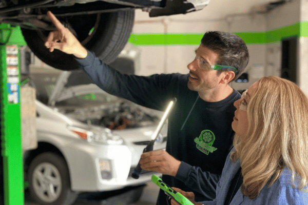 Electron Automotive technician explaining vehicle issue to customer under lift