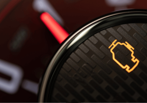 Close-up of illuminated check engine light on a car dashboard.