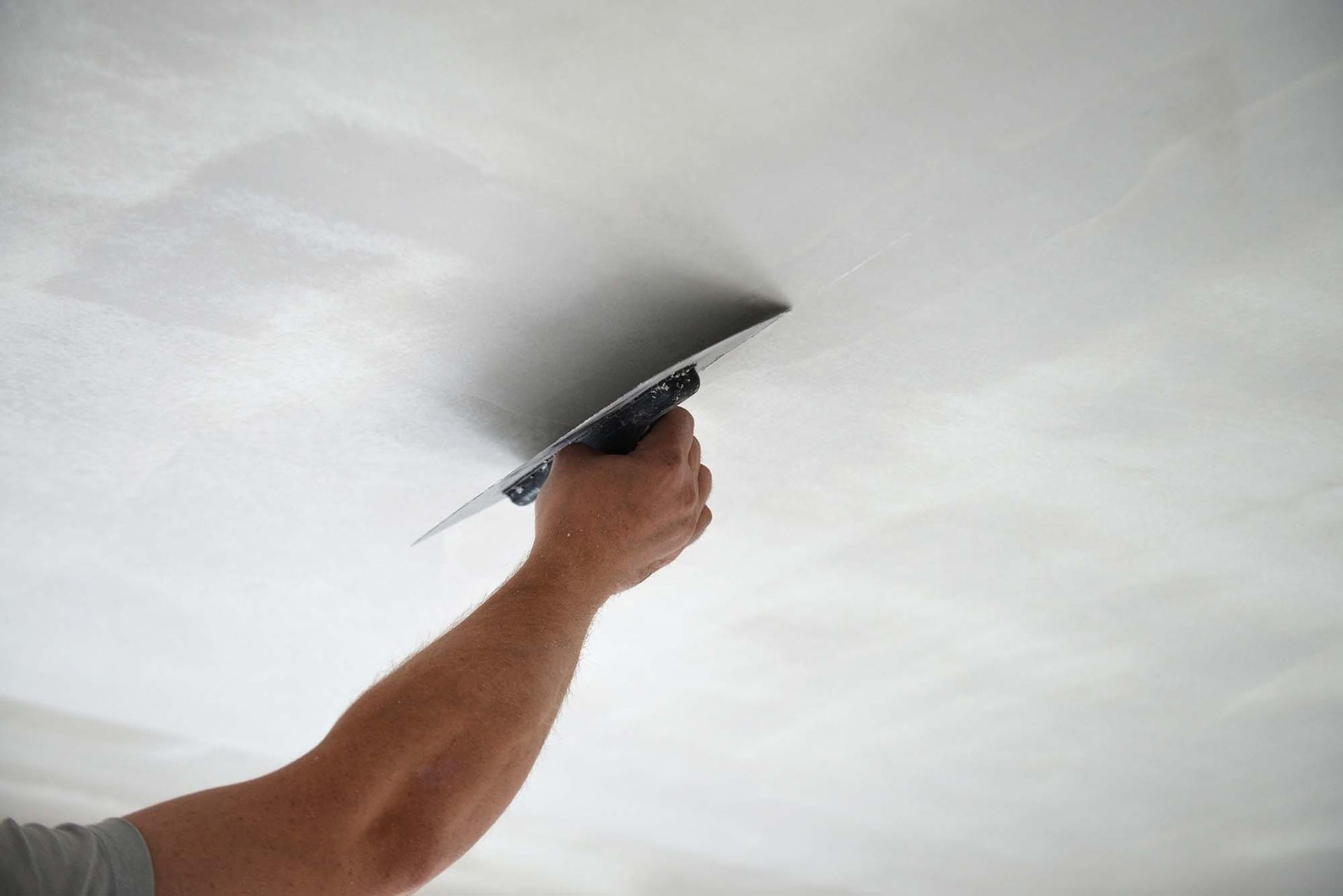 Hand smoothing wet plaster on a white ceiling with a trowel