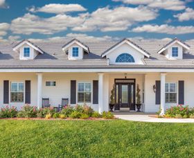White house with a blue roof, front porch, and flower bed under a partly cloudy sky
