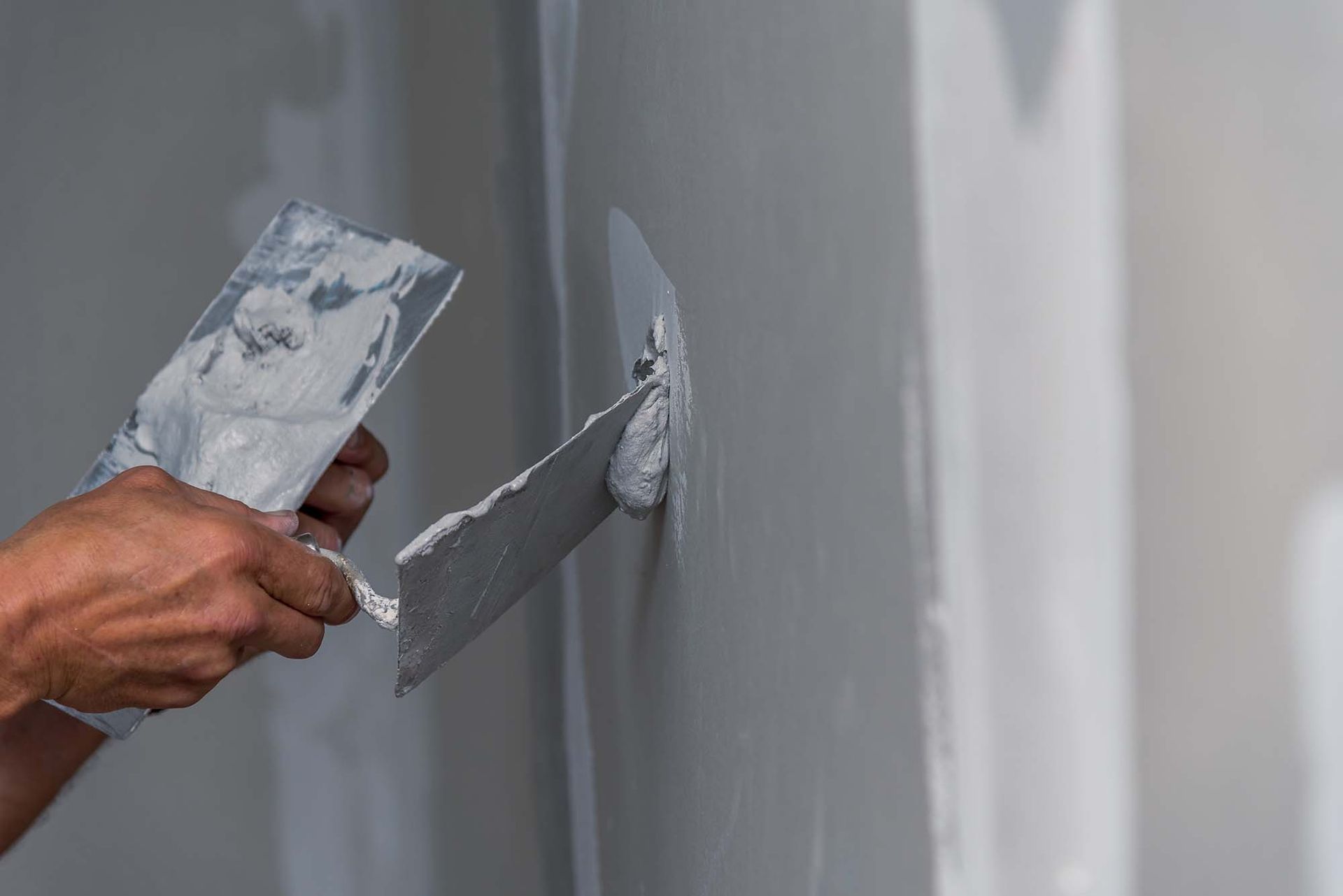 Hand spreading gray plaster on a wall with a putty knife