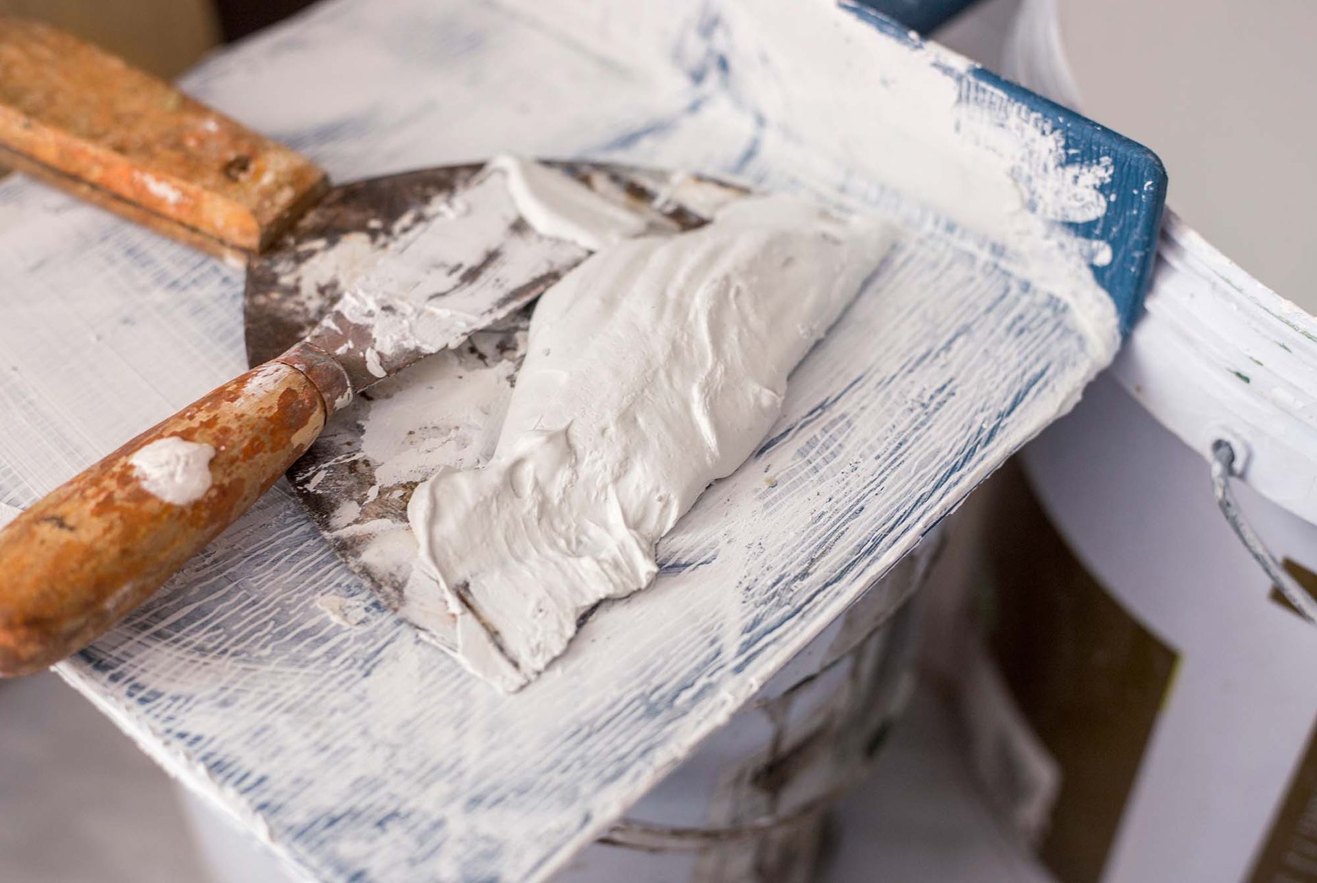 Putty knife spreading white compound on a painted wooden surface