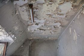 Peeling, water-damaged ceiling and walls in a small room, with exposed wood and crumbling plaster
