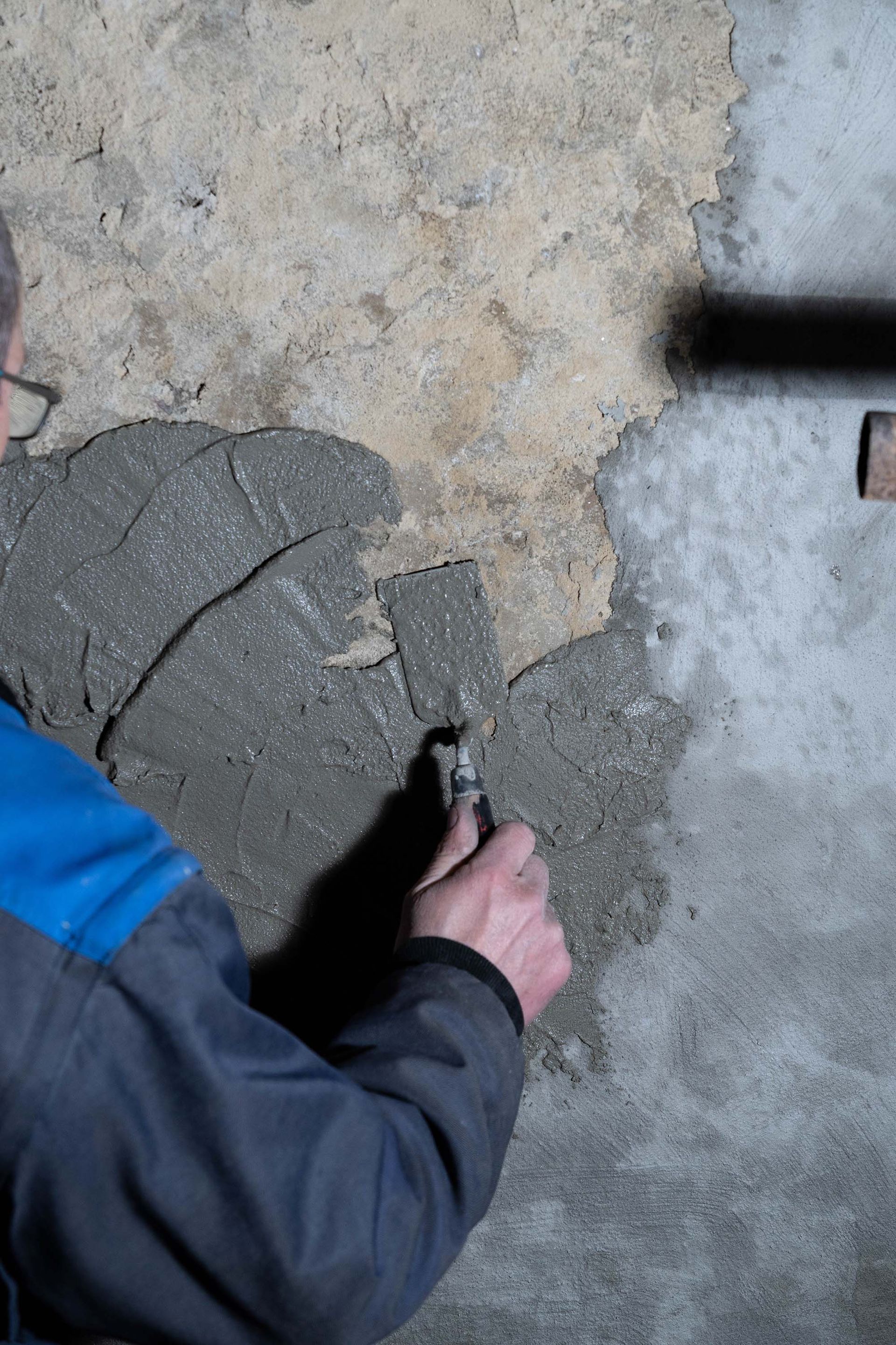 Person spreading gray mortar over a concrete floor with a trowel.