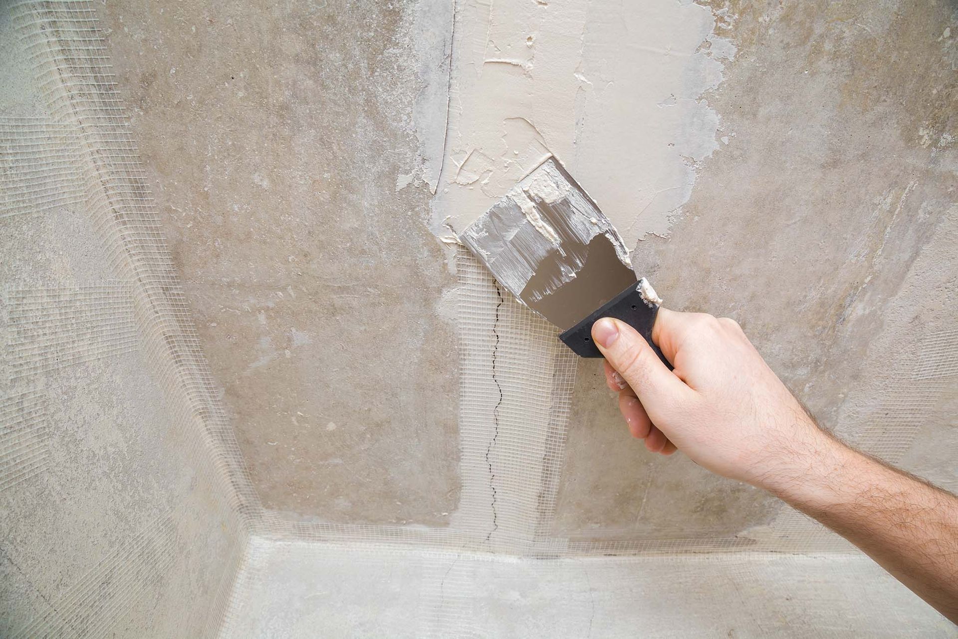 Hand spreading gray plaster on a wall with a putty knife