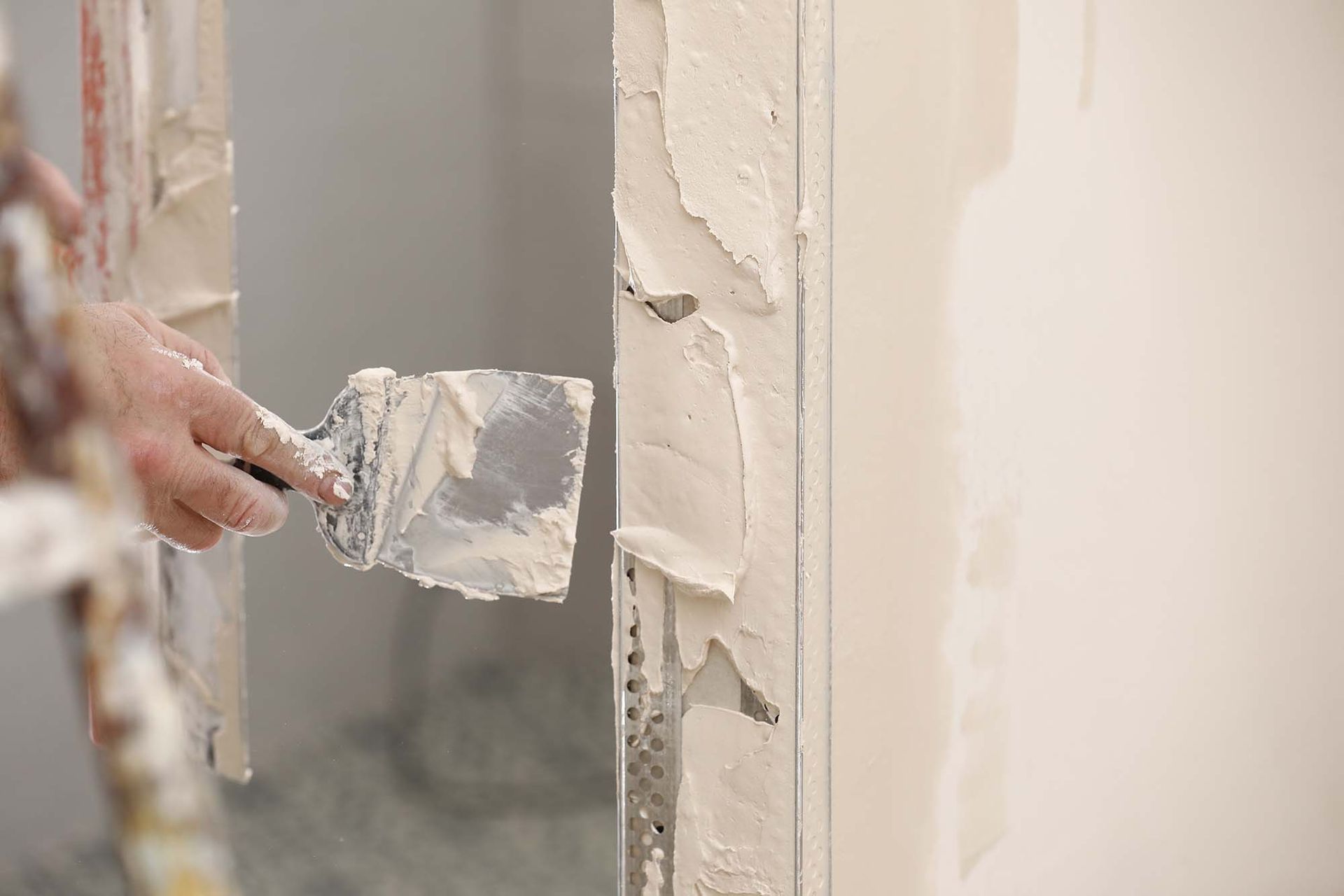 Hand spreading white plaster on a wall with a putty knife
