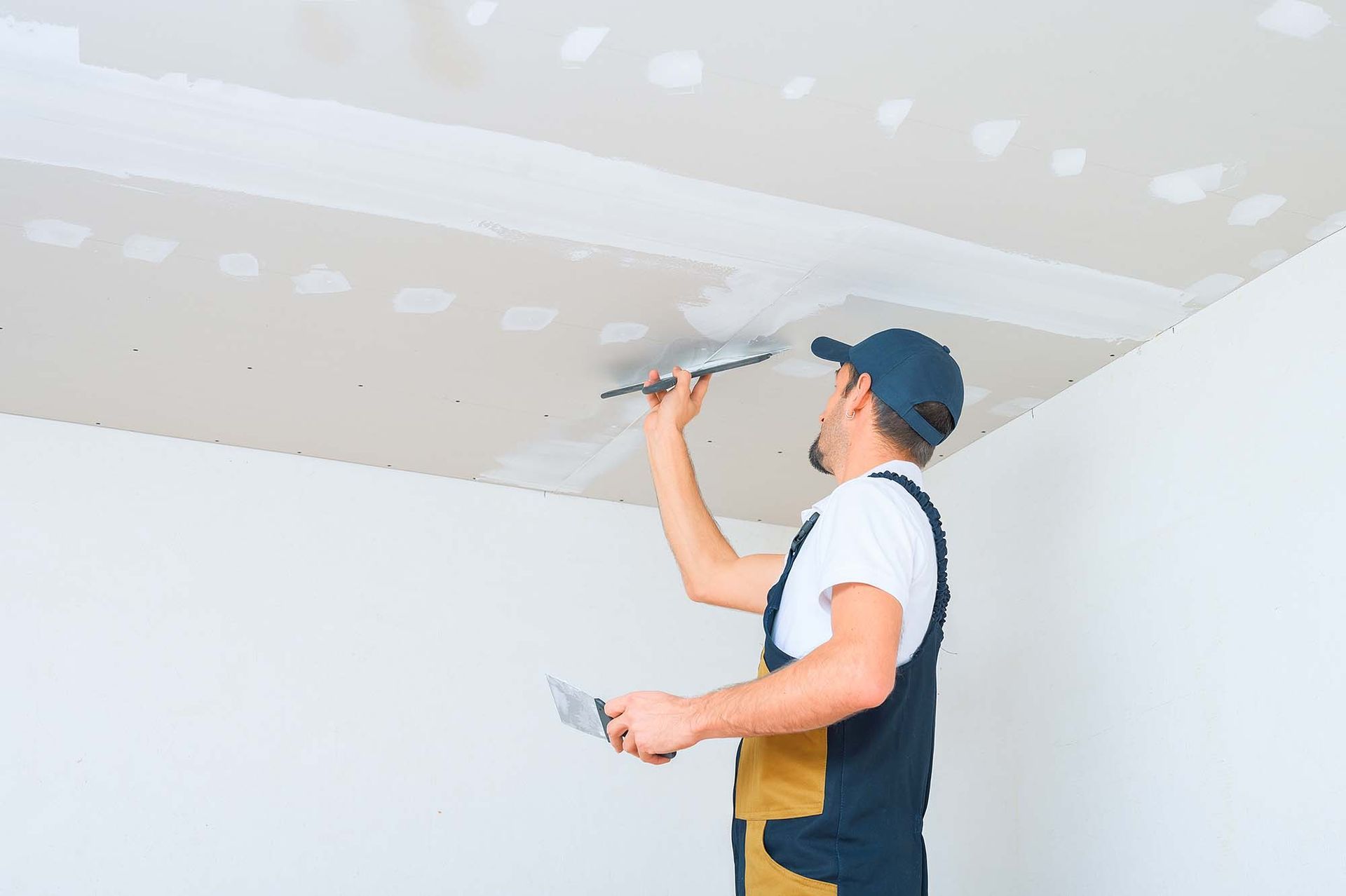 Worker applying drywall compound to a ceiling with a putty knife