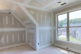 Empty beige bedroom with sloped ceiling, white trim, and a large window overlooking trees and water.