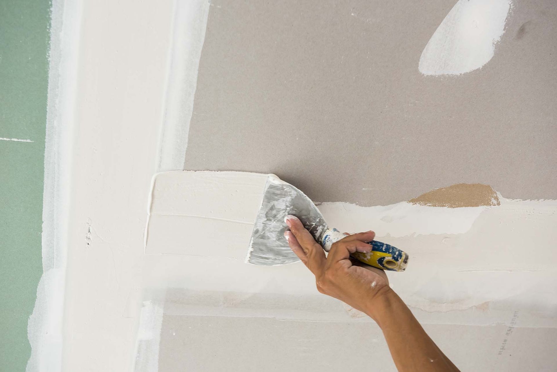 Hand sanding a white wall corner during interior painting or drywall finishing