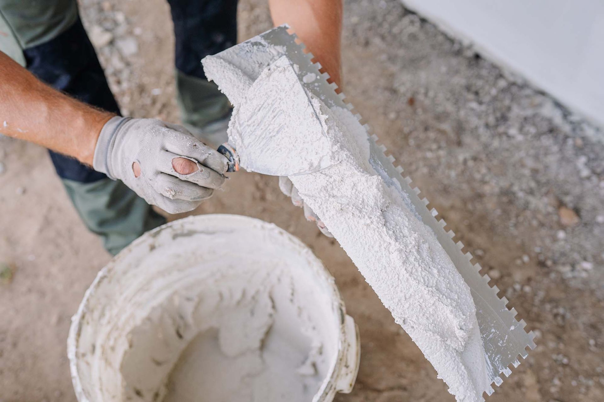 Hands applying white plaster to a wall with a trowel beside a bucket of compound.