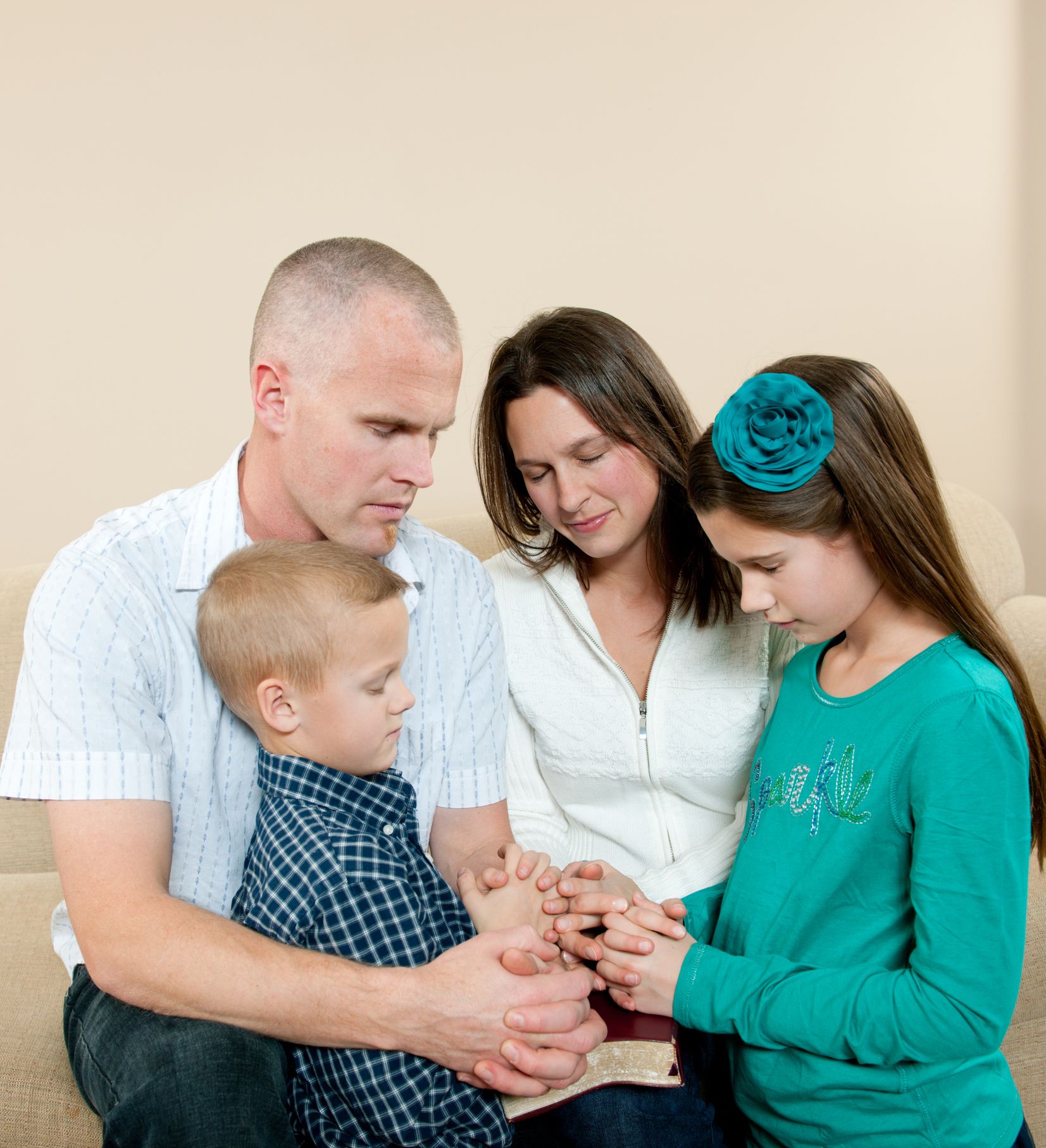 A family is sitting on a couch praying together