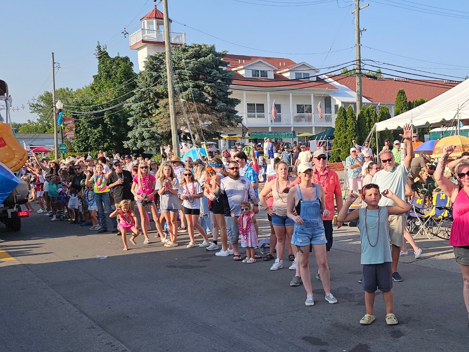 A large group of people are standing on a street in front of a lighthouse.