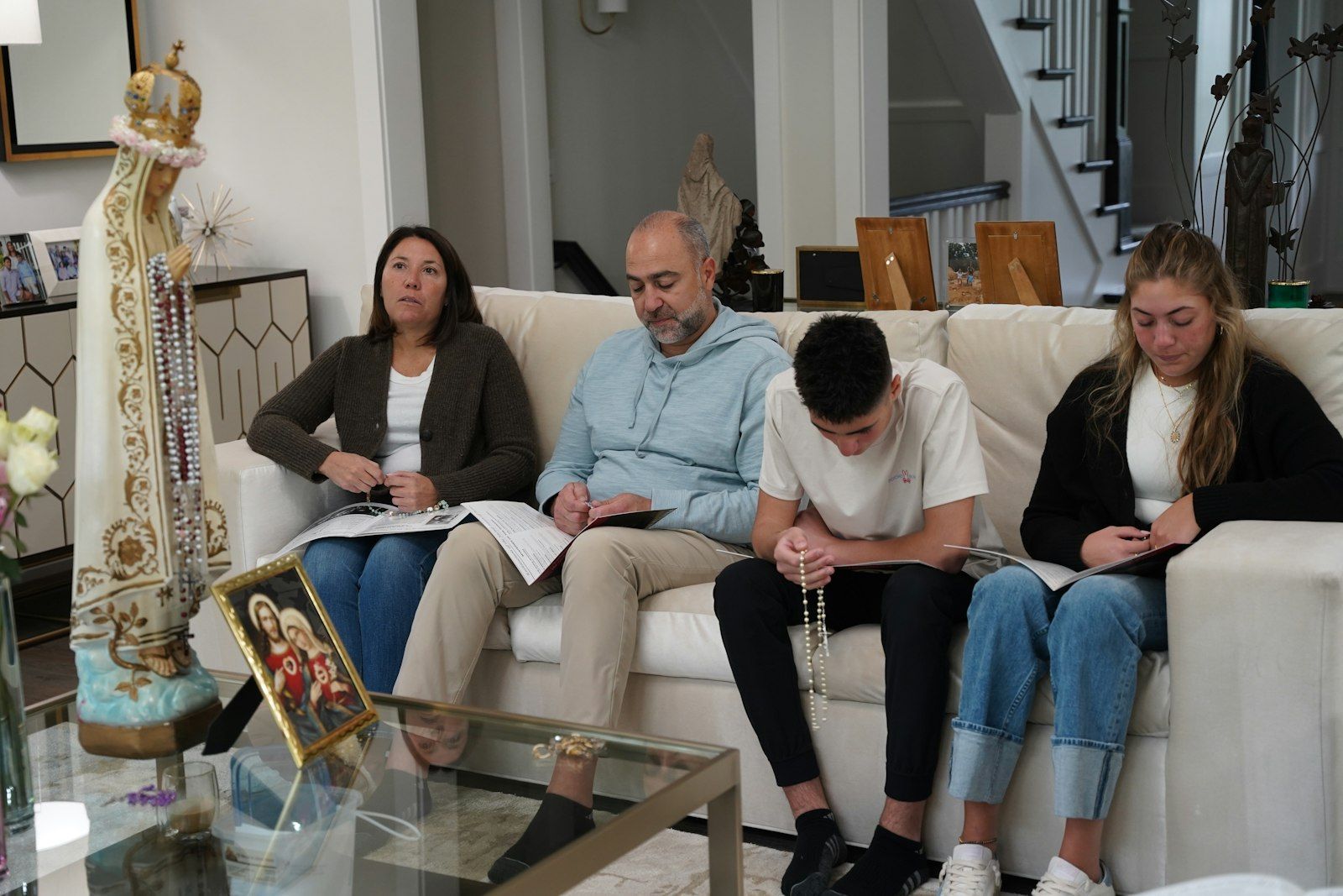 A family is sitting on a couch praying in a living room during home enthronement