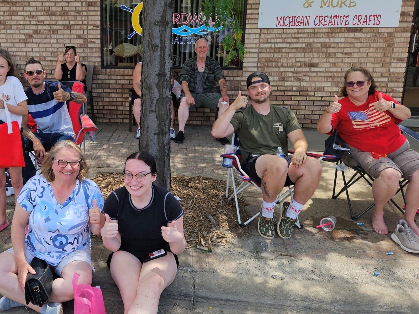 A group of people are sitting on the sidewalk giving a thumbs up