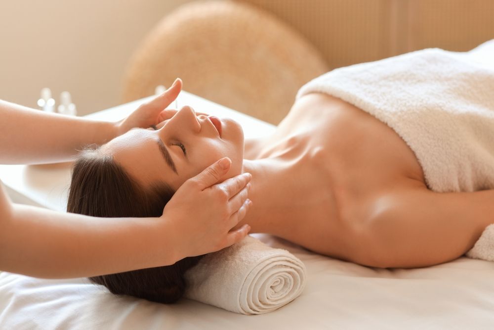 Person receiving a head massage on a spa table with a white towel and rolled towel under the head