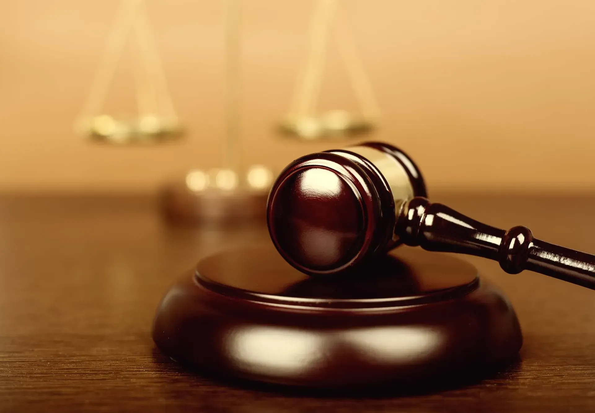 Wooden gavel on a stand with a balance scale in the background, set on a brown table.