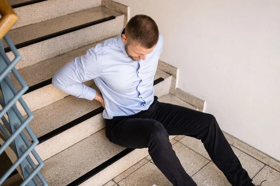 Man sitting on stairs, clutching his back, likely injured after a fall.