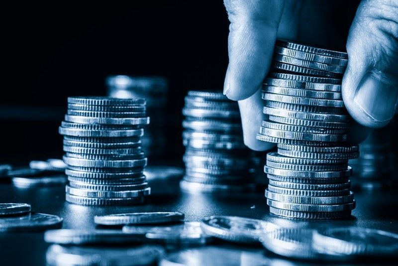 Hand stacking silver coins, with stacks of coins in the background.