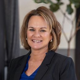 A woman wearing a blue shirt and earrings is smiling for the camera.