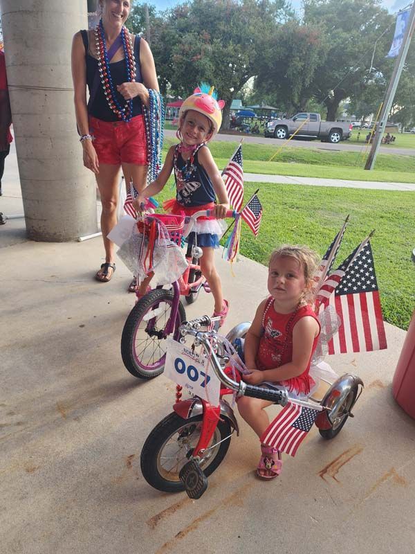 Two little girls are riding bicycles decorated with american flags