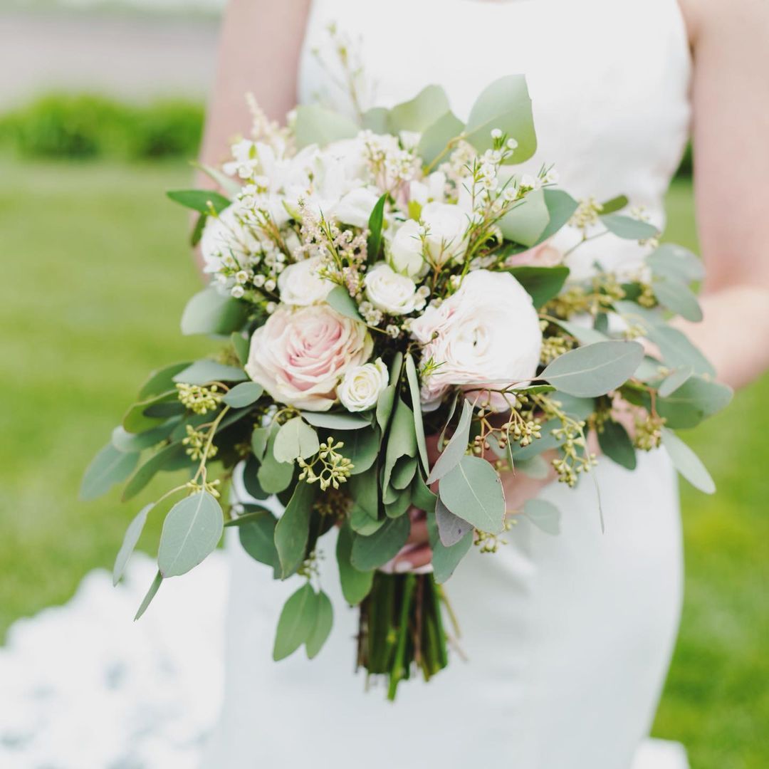 A bride in a white dress is holding a bouquet of white flowers