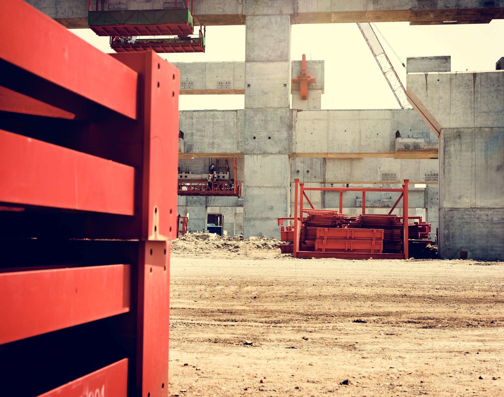 Orange construction barrier in foreground, with unfinished concrete building and dirt lot behind it