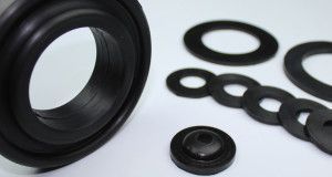 Un montón de anillos de goma negros y arandelas sobre una superficie blanca.